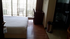 Ein Hotelzimmer mit einem Bett, einem Schreibtisch, einem Stuhl, einem Mülleimer und einem durch eine Glastür einsehbarer Badezimmer.