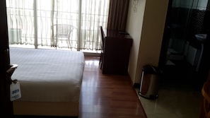 A hotel room with a bed, a desk, a chair, a trash bin, and a bathroom visible through a glass door. - Impress Hotel (Addis Ababa)