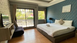 Une chambre d’hôtel moderne avec un grand lit, un téléviseur posé sur une console en bois, un balcon avec du mobilier d’extérieur et un mur orné d’un motif bleu.