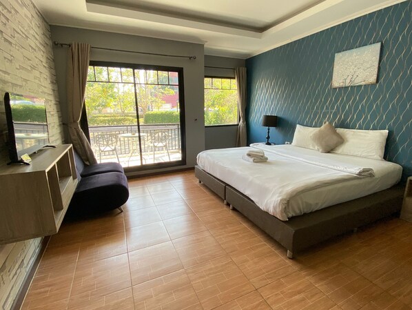A modern hotel room with a large bed, a TV on a wooden console, a balcony with outdoor furniture, and a blue patterned wall.