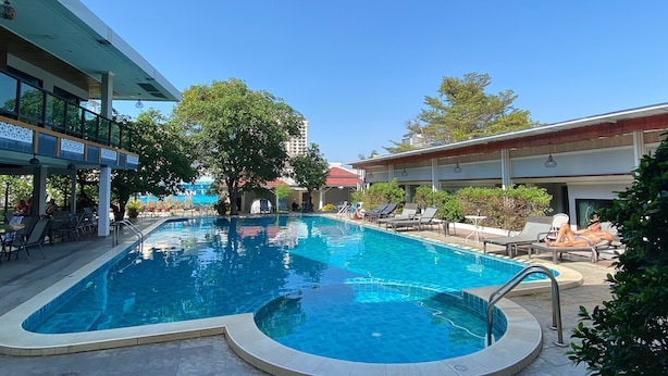 Une piscine à bordures incurvées, entourée de chaises longues et dotée d’un espace salon abrité.
