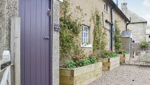 A stone building with a purple door, wooden planters, and a gravel driveway. - Cuthbert House - UK7026 (Longframlington, near Rothbury)