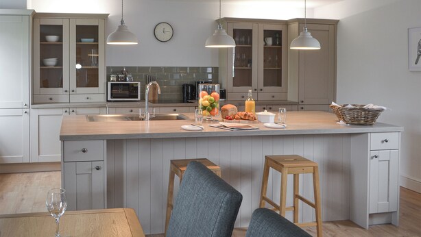 A modern kitchen with a central island, wooden stools, and pendant lighting. - Cuthbert House - UK7026 (Longframlington, near Rothbury)