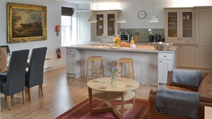 A modern kitchen with a central island, wooden chairs, a dining table, and a red rug. - Cuthbert House - UK7026 (Longframlington, near Rothbury)