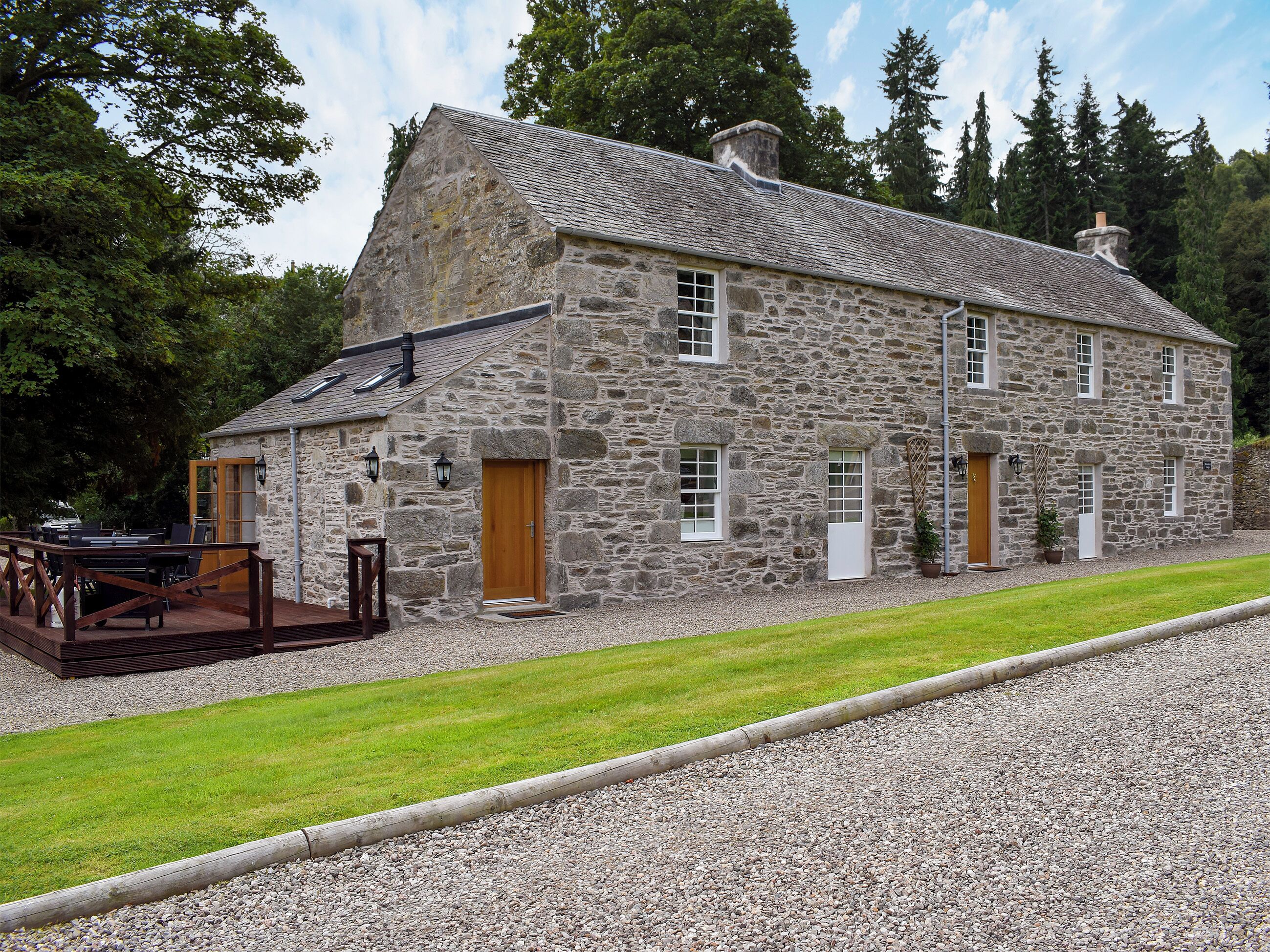 A stone building with a wooden deck and a gravel driveway.