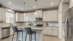 Uma cozinha com armários brancos, bancada de granito, eletrodomésticos de aço inoxidável e uma ilha grande com banquetas.
