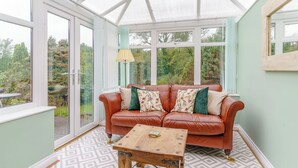 A conservatory with a leather sofa, a wooden coffee table, and patterned flooring. - Ivy Cottage - UK35243 (Llanfyrnach)