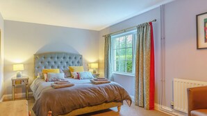 A bedroom with a large bed, bedside lamps, a window with curtains, a radiator, and a wooden chair. - Ivy Cottage - UK35243 (Llanfyrnach)