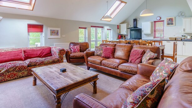 A spacious living room with leather sofas, a wooden coffee table, and a kitchen in the background. - The Coach House - UK35246 (Llanfyrnach)