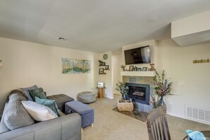 A living room with a gray sofa, ottoman, and a blue chair. There is a fireplace with a mantel, a flat-screen TV mounted above it, and a clock on the wall. - Pool Access + Balcony: Updated Condo Near UCSD! (San Diego)