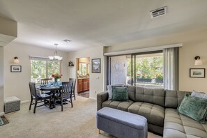 A spacious living room with a large sectional sofa, a dining table with chairs, and a kitchen area visible through an open sliding door. - Pool Access + Balcony: Updated Condo Near UCSD! (San Diego)