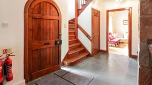 Une porte en bois, un escalier et un salon avec un fauteuil rose.