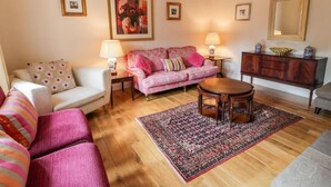 Un salon comprenant un canapé, un fauteuil, une table basse, un tapis, un meuble et des tableaux encadrés accrochés au mur.