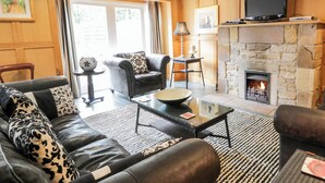 A living room with a stone fireplace, leather sofas, a glass coffee table, and a television on a wooden shelf. - Coach House - UK7236 (Kirkmichael, near Ayr)