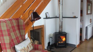 Ein gemütliches Wohnzimmer mit einem Karosessel, einem Kamin und einer Holzbalkendecke.