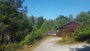 Ein rustikales Blockhaus mit Kiesweg, umgeben von dichtem Wald und einem Berg im Hintergrund.