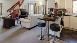 Een moderne keuken met witte kastjes, een eethoek met een tafel en stoelen, en een woonkamer met een bank en een televisie.