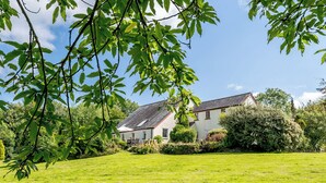Een huis met schuin dak, omgeven door een verzorgd gazon en weelderige begroeiing.