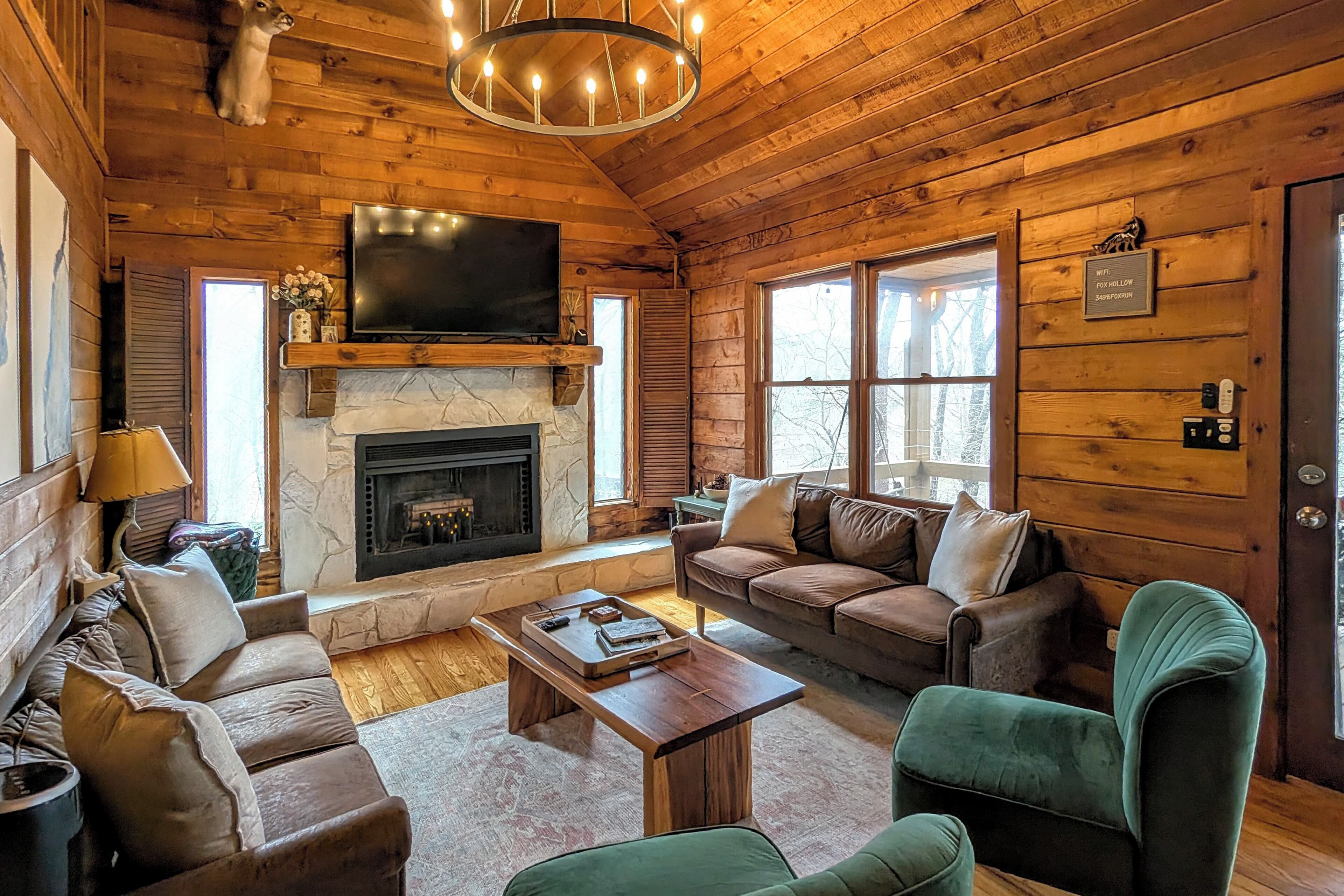 Interior acogedor de una cabaña con chimenea, paredes de madera, un televisor y un sofá.