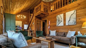 Ein Blockhaussalon mit einer Holztreppe, einem Essbereich und einem Wohnzimmer mit Sofa und Couchtisch.
