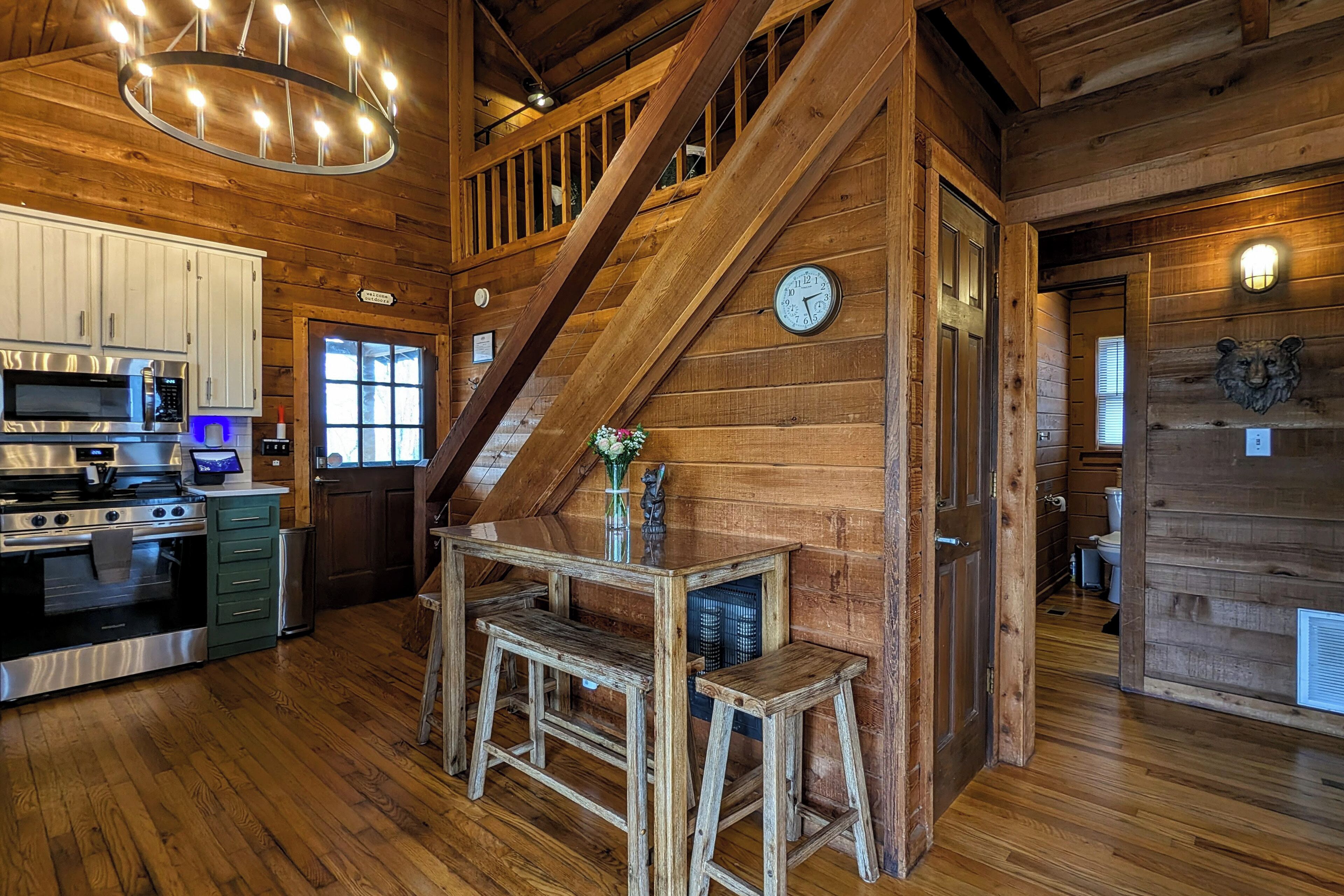 A wooden cabin interior with a kitchen, dining area, and staircase.