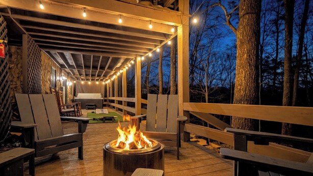 Eine Terrasse im Freien mit Feuerstelle, Holzmöbeln und Lichterketten.