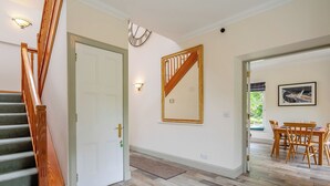 Un escalier avec des rampes en bois, une porte blanche, un miroir fixé au mur, un coin repas avec une table et des chaises, et un sol à motifs.