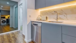 A modern kitchen with grey cabinets, a stainless steel dishwasher, a marble backsplash, and a built-in oven. - Vita Portucale | Alfama Sweet Retreat (Lisboa)