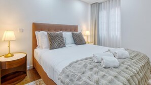 A modern hotel room with a large bed, two bedside tables with lamps, a fluffy throw blanket, and a view of the city through sheer curtains. - Vita Portucale | Alfama Sweet Retreat (Lisboa)