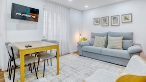 A modern living room with a dining area, a grey sofa, and a TV mounted on the wall. - Vita Portucale | Alfama Sweet Retreat (Lisboa)