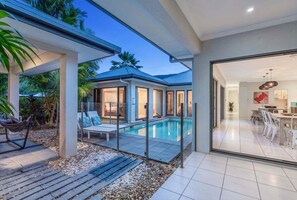 Ein modernes Haus mit Schwimmbad, überdachter Terrasse und Essbereich.