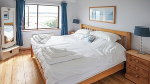 A bedroom with a wooden bed, a bedside table with a lamp, a dresser, a window with curtains, and a framed picture on the wall. - Sea Breeze at Fishermans Dock (Poole)