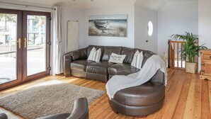 A modern living room with a leather sofa, a wooden floor, a large window with curtains, a painting on the wall, and a potted plant. - Sea Breeze at Fishermans Dock (Poole)