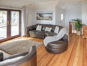A modern living room with a leather sofa, a wooden floor, a large window with curtains, a painting on the wall, and a potted plant. - Sea Breeze at Fishermans Dock (Poole)
