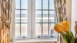 A window with a view of the beach and a potted plant with yellow flowers. - 2 bedroom accommodation in Sandsend, near Whitby (Sandsend, near Whitby)