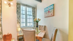 A dining area with a wooden table, two upholstered chairs, a vase with flowers, a clock, and a painting on the wall. - 2 bedroom accommodation in Sandsend, near Whitby (Sandsend, near Whitby)