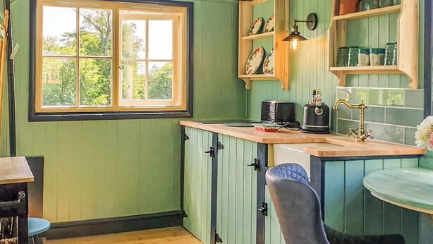 Een keuken met groene wanden, een raam, een spoelbak en een waterkoker.