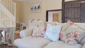 A living room with a sofa, floral cushions, a painting, and a wooden door. - 3 bedroom accommodation in Portway (Portway)