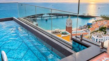 Piscina com guarda-vidro de vidro e vista para uma paisagem urbana costeira, incluindo uma torre do relógio imponente.