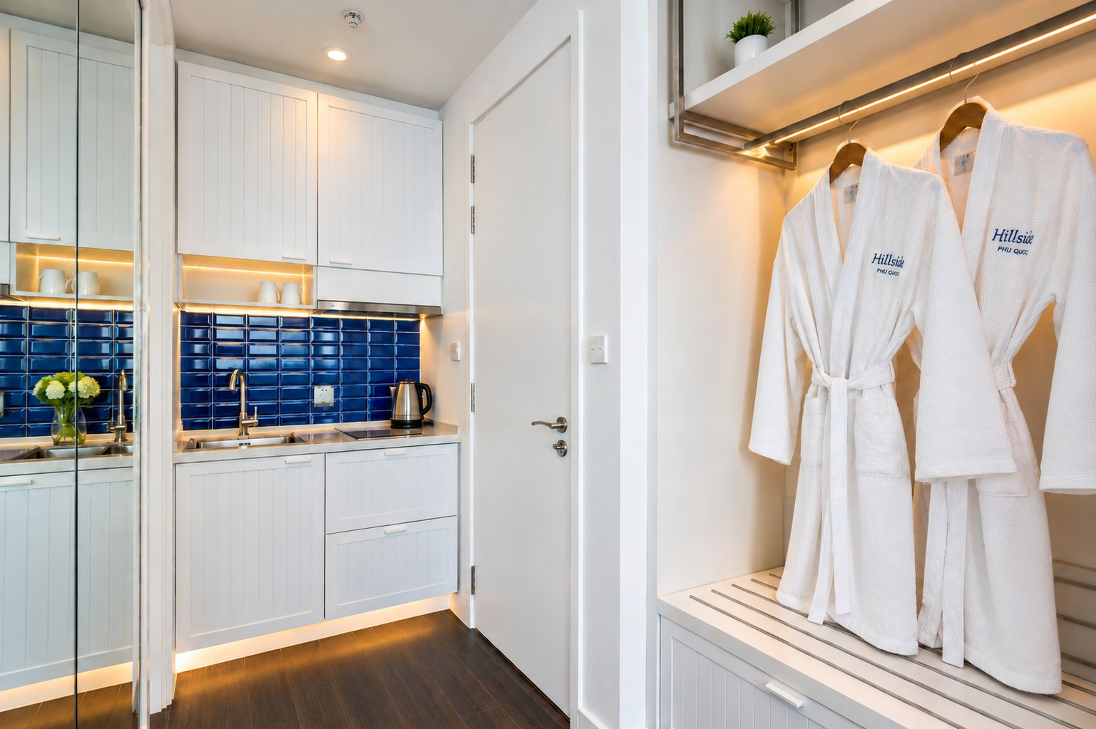 A modern bathroom with white cabinets, a blue tiled backsplash, and a robe rack with two white robes.