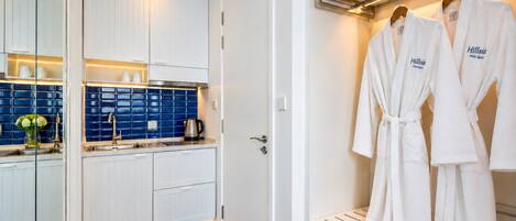 A modern bathroom with white cabinets, a blue tiled backsplash, and a robe rack with two white robes.