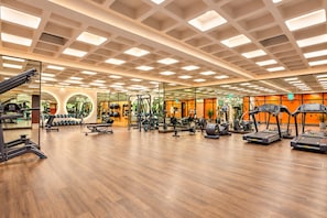 Un gimnasio con diversos equipos de ejercicio, suelo de madera y pared con espejos.