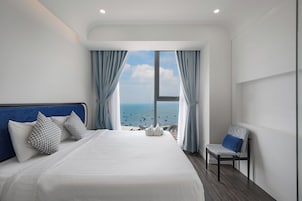 Quarto de hotel com uma cama grande, uma cadeira e vista para o mar.