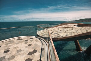 Una terraza con piso estampado, barandal de vidrio y vista al mar.