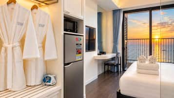 Ein Hotelzimmer mit Bett, Minibar, Kühlschrank, Fernseher und Blick auf den Sonnenuntergang über dem Wasser.