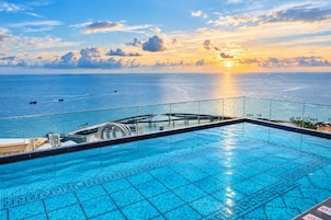 A swimming pool with a view of the sea and a sunset.