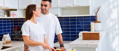 A couple in a kitchen with white cabinets, a blue backsplash, and a basket on the counter.