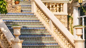 A staircase with blue and yellow patterned tiles, flanked by columns and a balustrade, leading to a building with a stone facade.