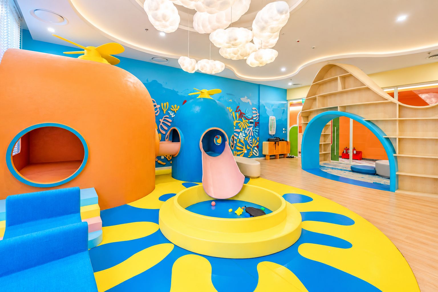 Espaço infantil com escorrega, estruturas de escalada e um mural colorido.