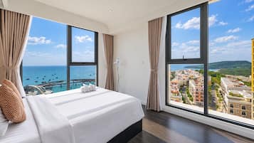 Een hotelkamer met een groot bed, twee ramen en uitzicht op zee en de stad.